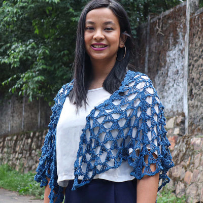 A Women wearing a blue knitted silk scarf from eri silk in the side of the road. Download this beautiful silk knitting pattern online from Muezart